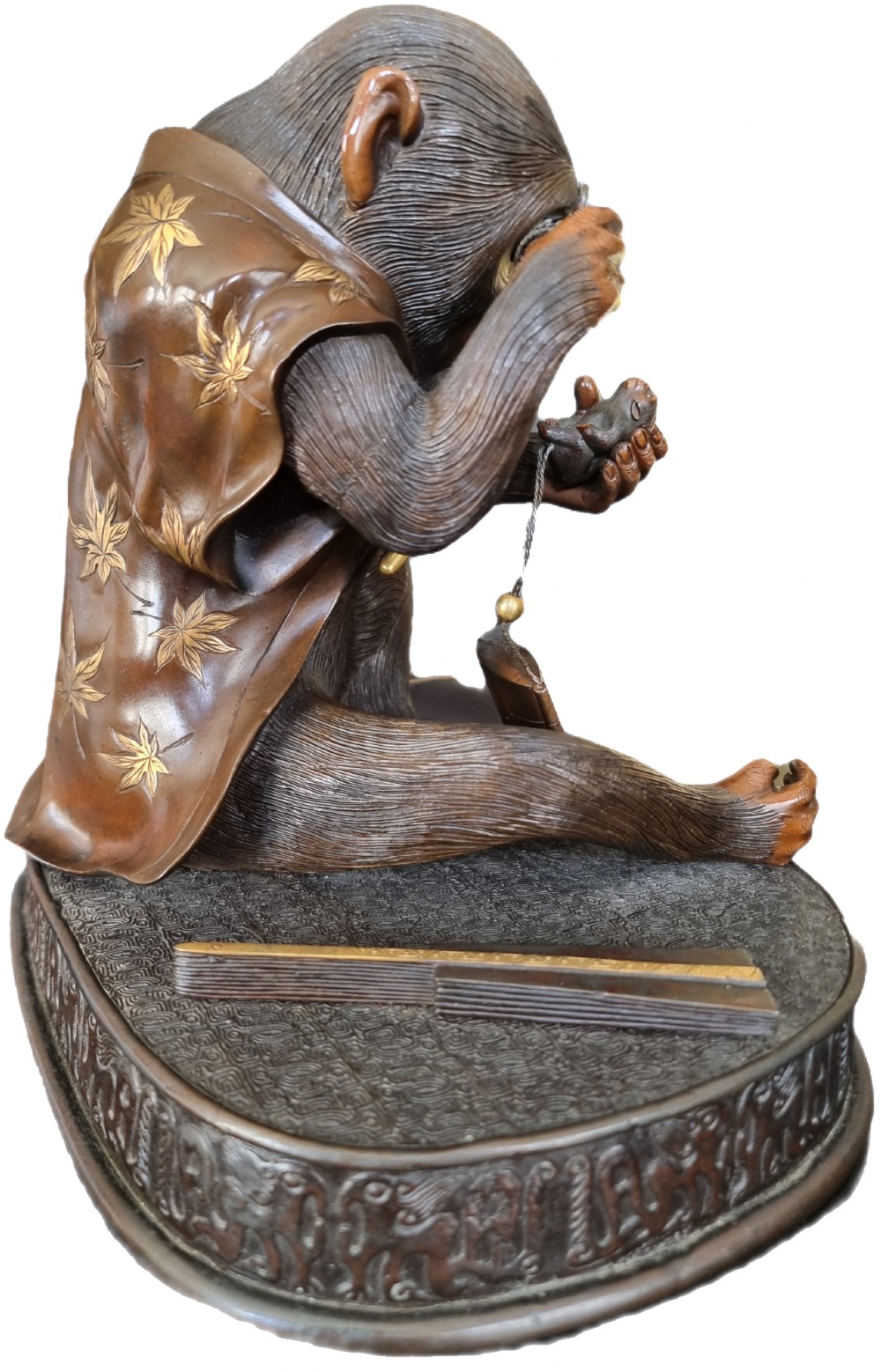 A dark bronze Japanese okimono sculpture depicting an anthropomorphic monkey wearing spectacles, seated with a book and inro. View II