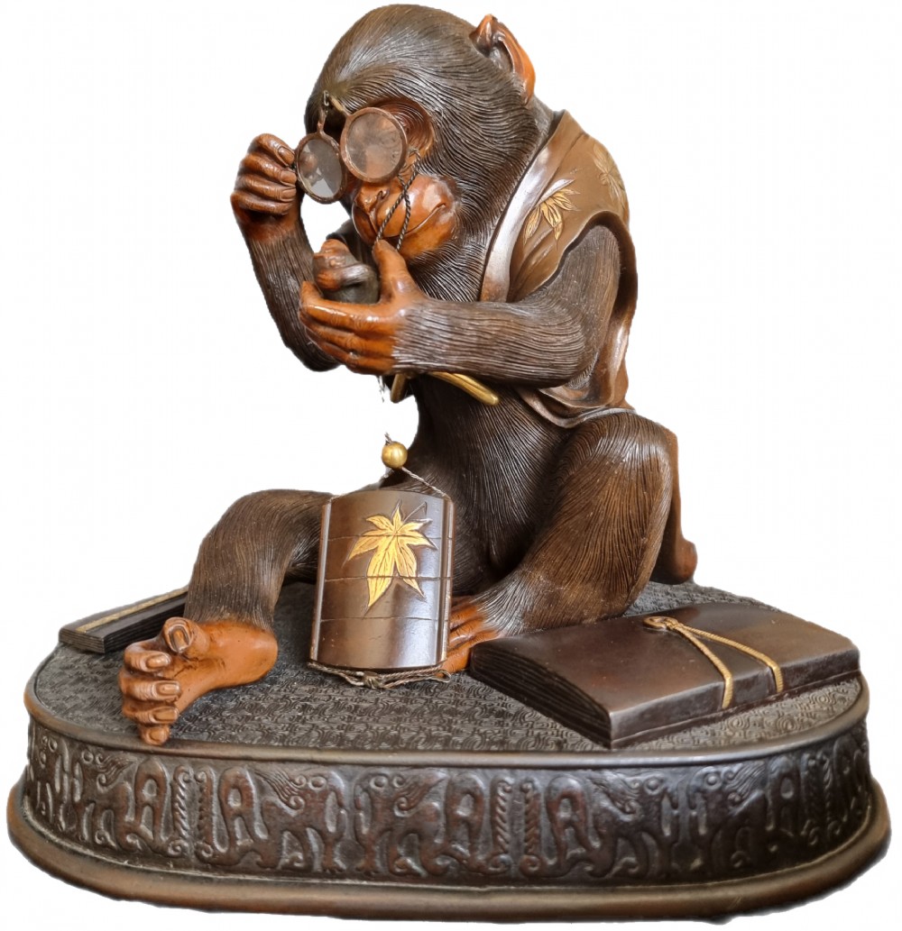 A dark bronze Japanese okimono sculpture depicting an anthropomorphic monkey wearing spectacles, seated with a book and inro. View IV