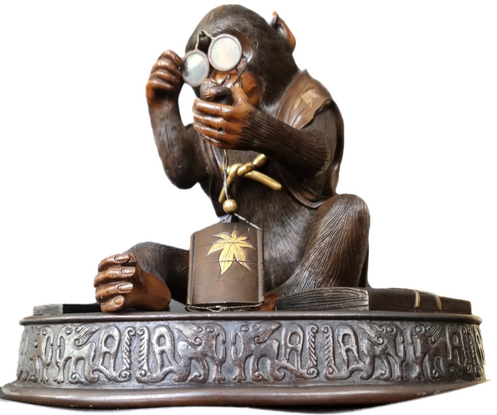 A dark bronze Japanese okimono sculpture depicting an anthropomorphic monkey wearing spectacles, seated with a book and inro. View V