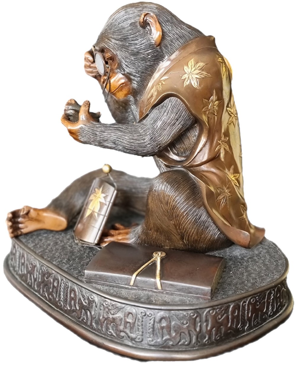 A dark bronze Japanese okimono sculpture depicting an anthropomorphic monkey wearing spectacles, seated with a book and inro. View VI