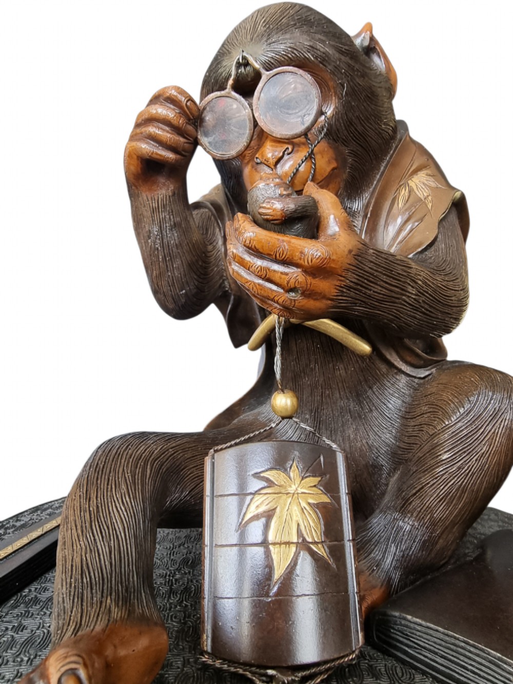 A dark bronze Japanese okimono sculpture depicting an anthropomorphic monkey wearing spectacles, seated with a book and inro. View VII