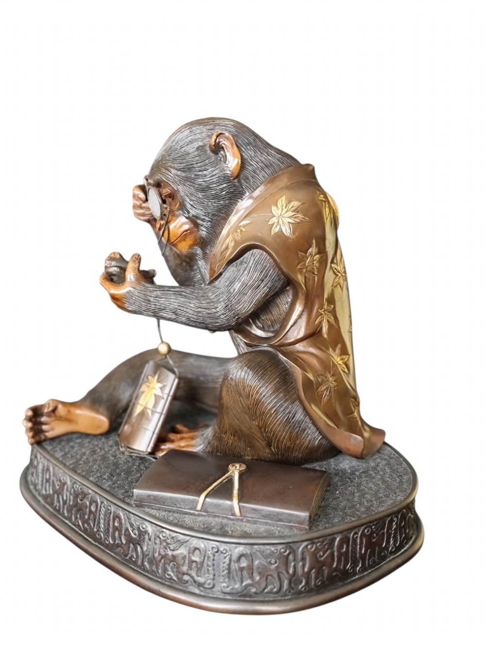 A dark bronze Japanese okimono sculpture depicting an anthropomorphic monkey wearing spectacles, seated with a book and inro. View X