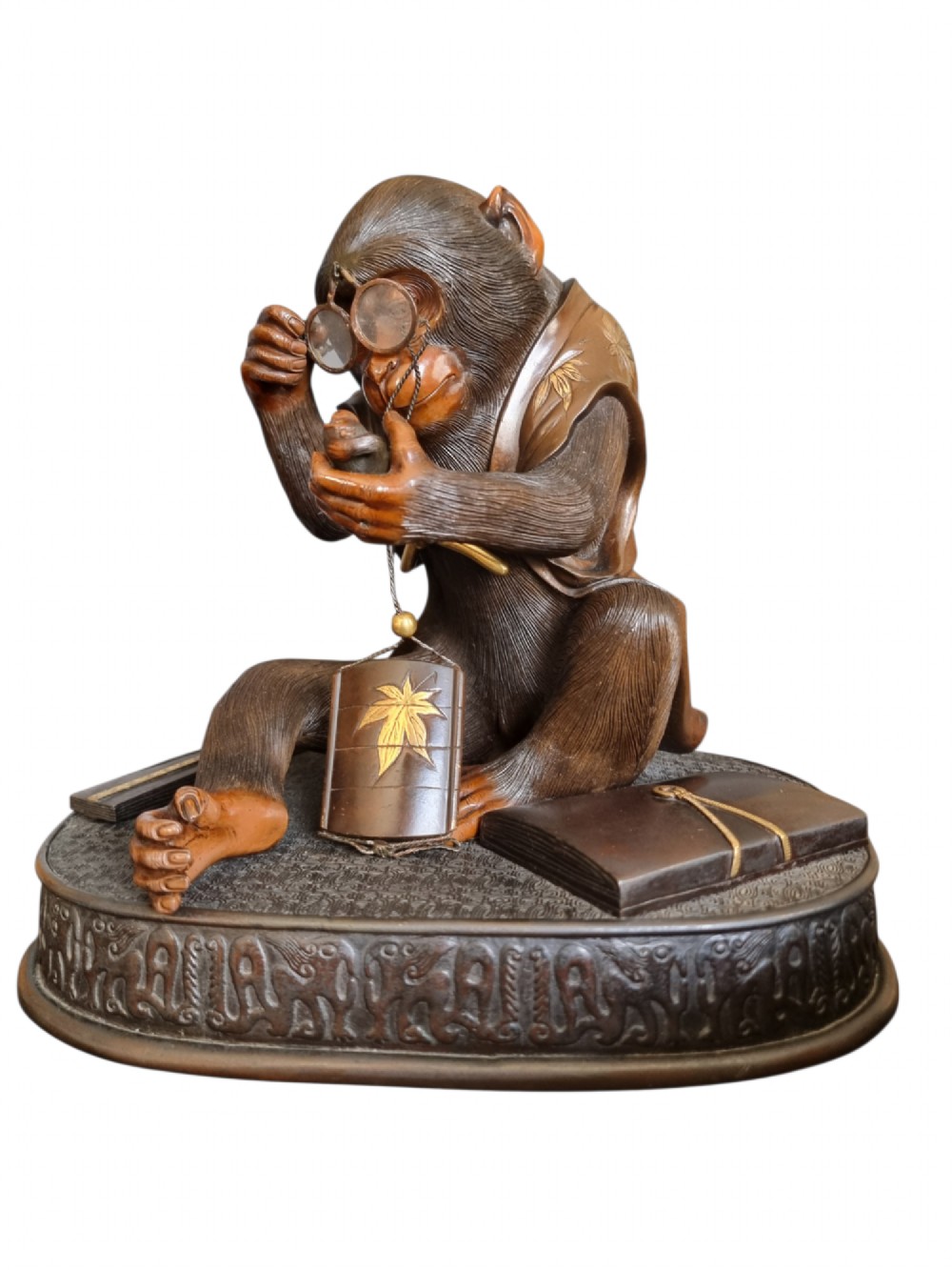 A dark bronze Japanese okimono sculpture depicting an anthropomorphic monkey wearing spectacles, seated with a book and inro. View XII