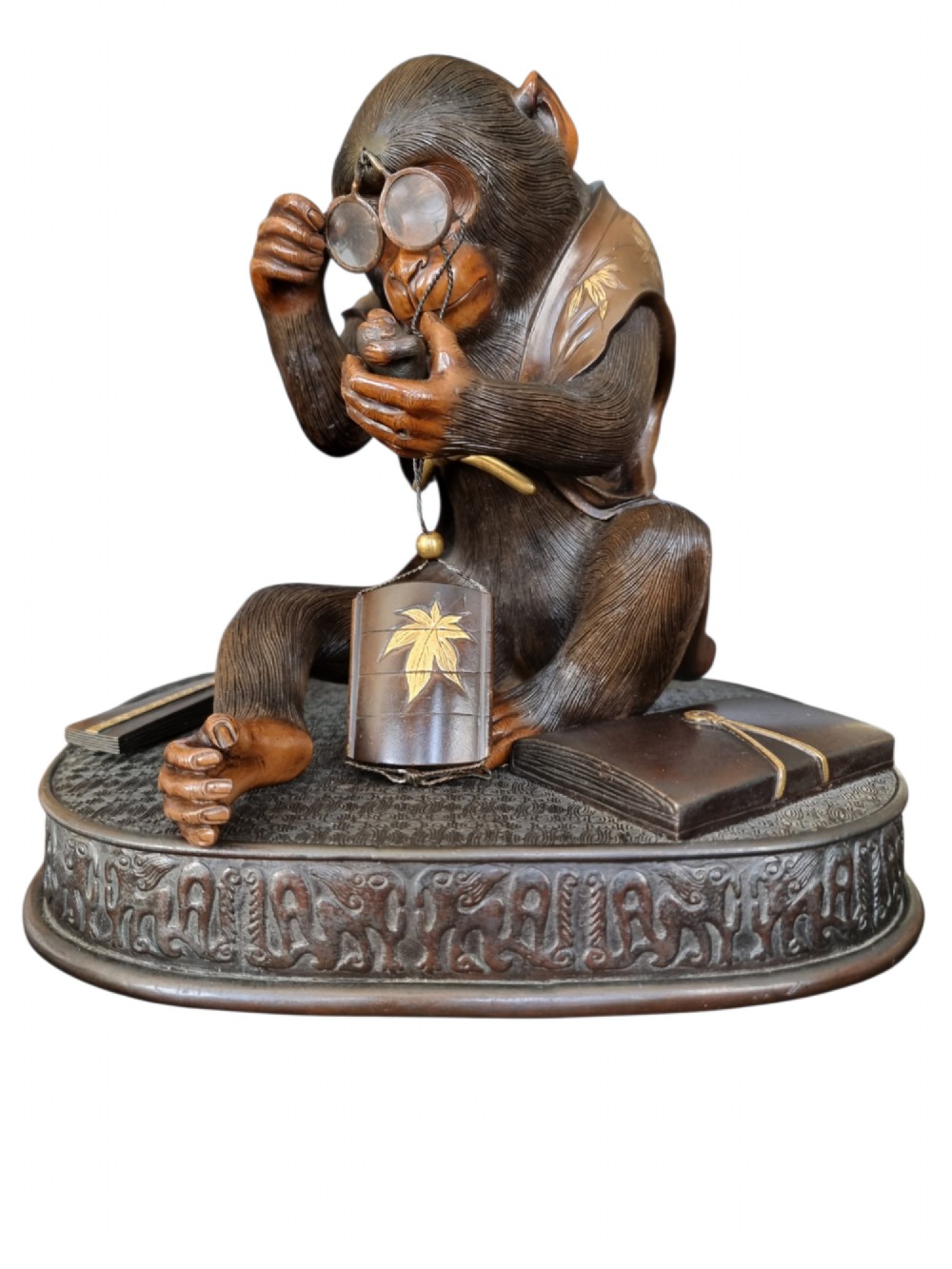 A dark bronze Japanese okimono sculpture depicting an anthropomorphic monkey wearing spectacles, seated with a book and inro. View XIII
