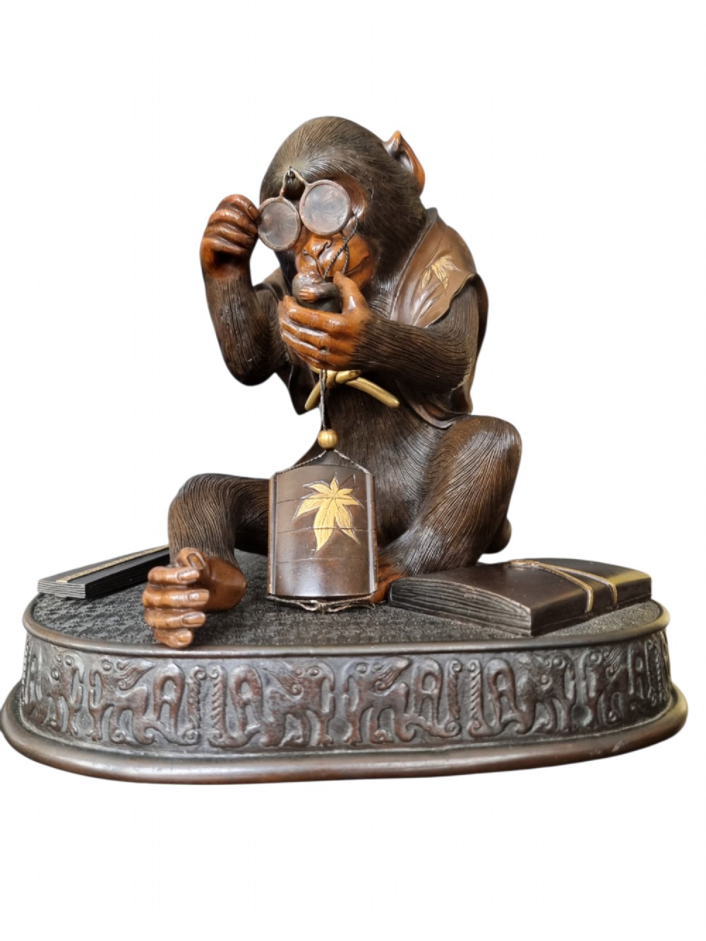 A dark bronze Japanese okimono sculpture depicting an anthropomorphic monkey wearing spectacles, seated with a book and inro. View XV