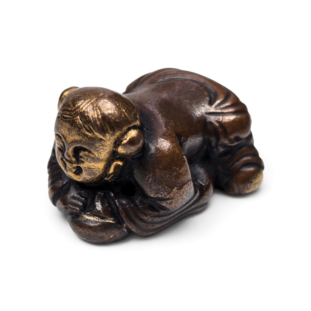 A dark bronze cast sculpture of a reclining child with gilded details on the head and face, resting on a flat base. View II