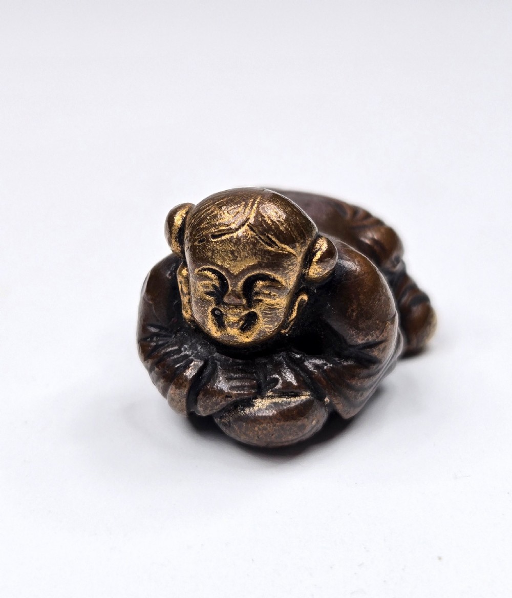A dark bronze cast sculpture of a reclining child with gilded details on the head and face, resting on a flat base. View III