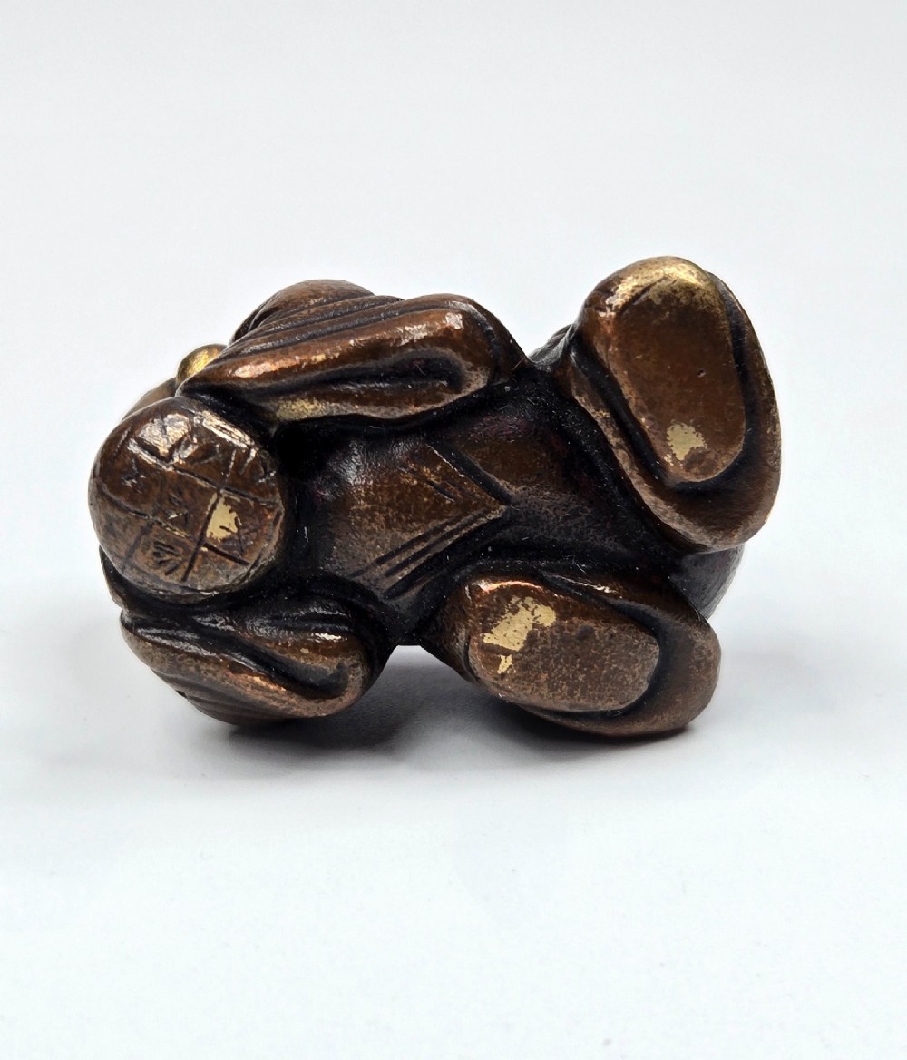 A dark bronze cast sculpture of a reclining child with gilded details on the head and face, resting on a flat base. View V