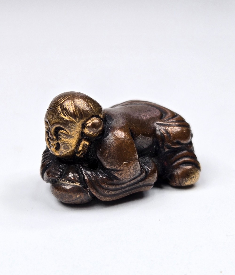 A dark bronze cast sculpture of a reclining child with gilded details on the head and face, resting on a flat base. View VI