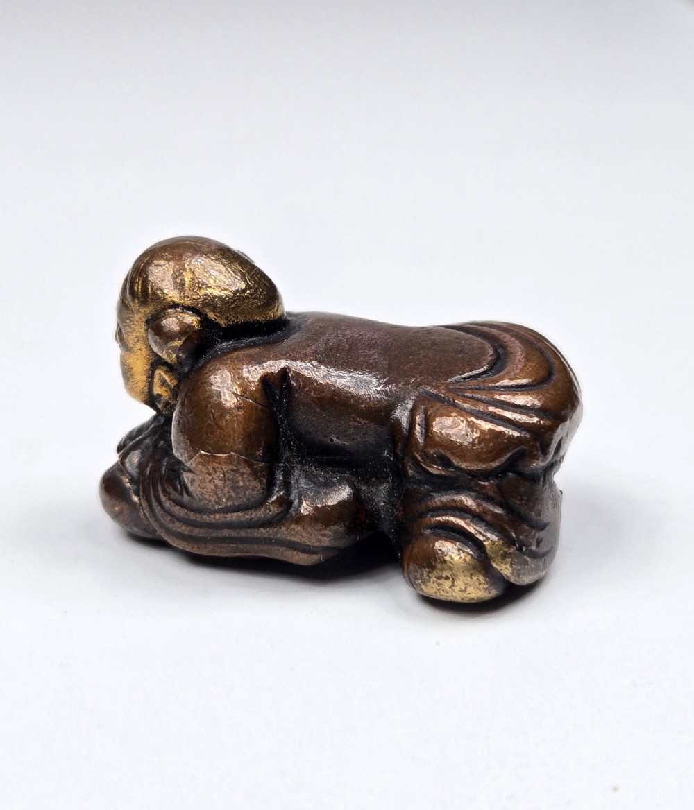 A dark bronze cast sculpture of a reclining child with gilded details on the head and face, resting on a flat base. View VII