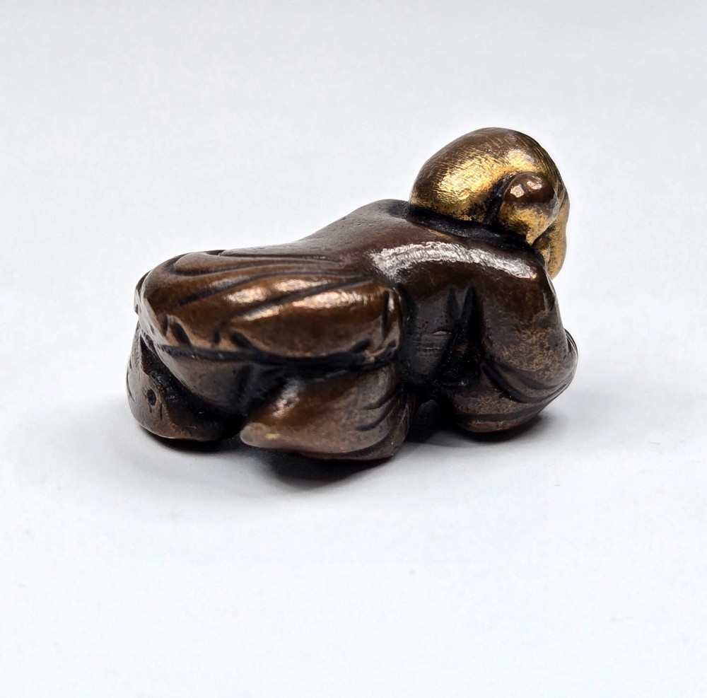 A dark bronze cast sculpture of a reclining child with gilded details on the head and face, resting on a flat base. View IX