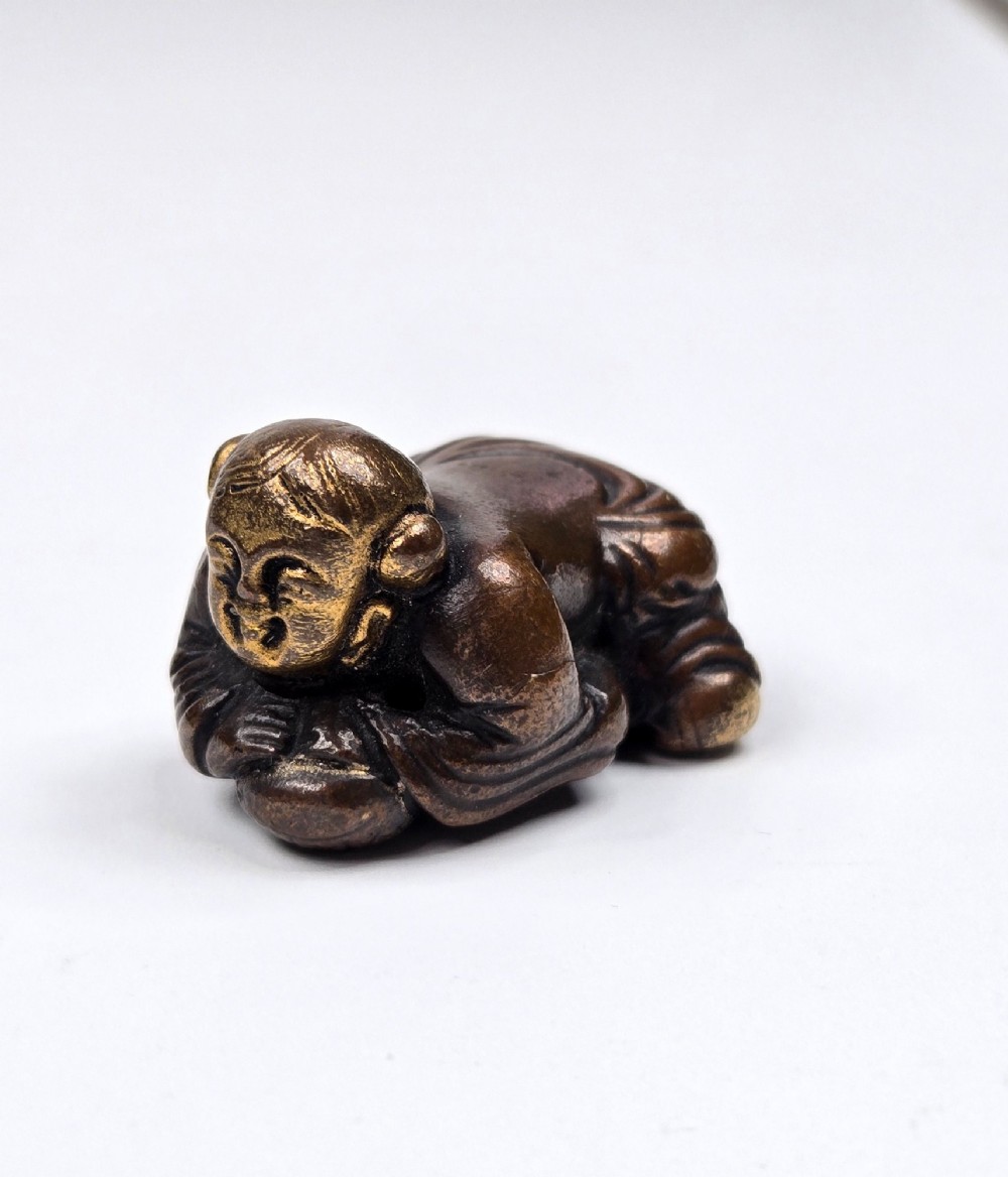 A dark bronze cast sculpture of a reclining child with gilded details on the head and face, resting on a flat base. View XI