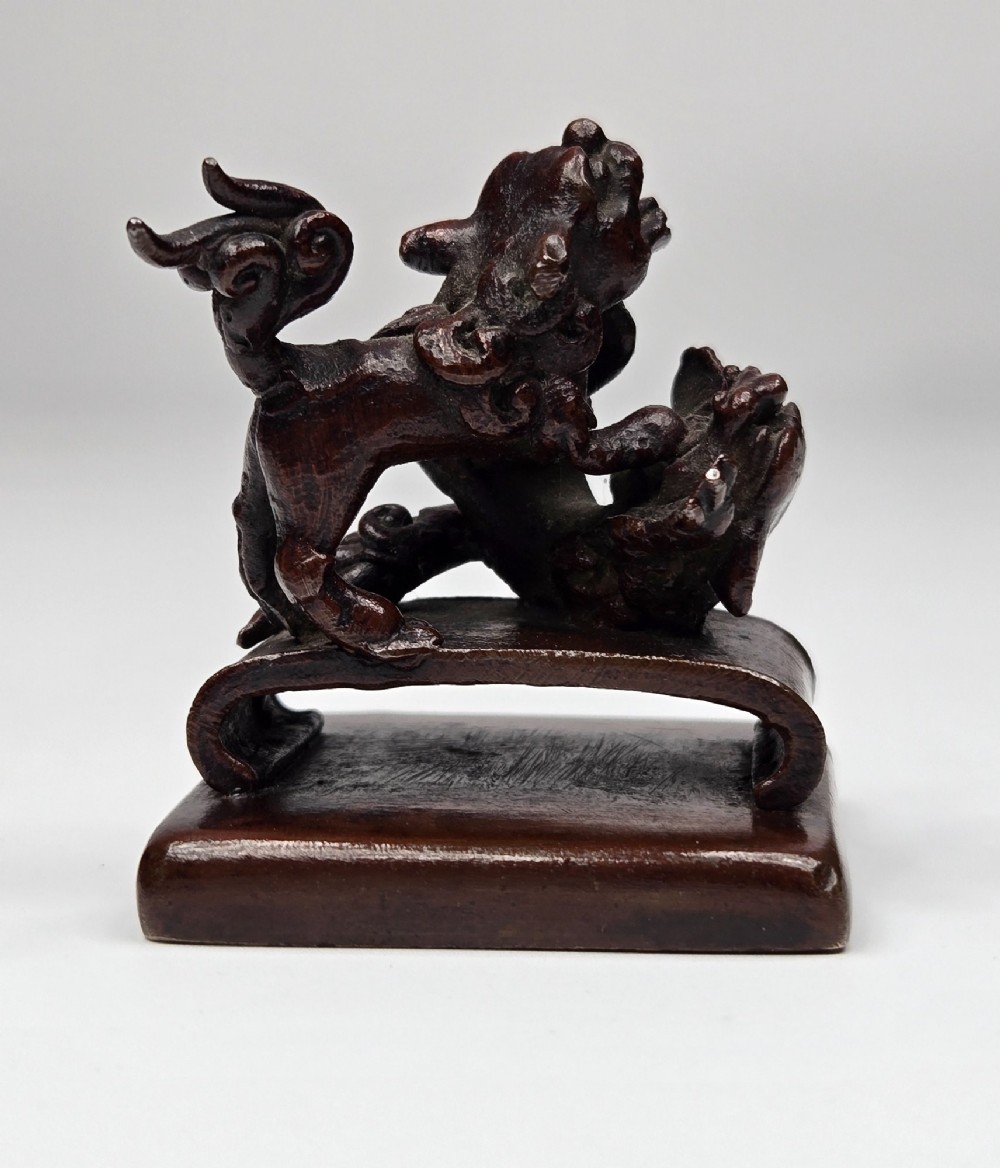 A dark bronze Chinese scholars seal topped with two sculptural wrestling shishi lions resting on an arched platform atop a square base. View III