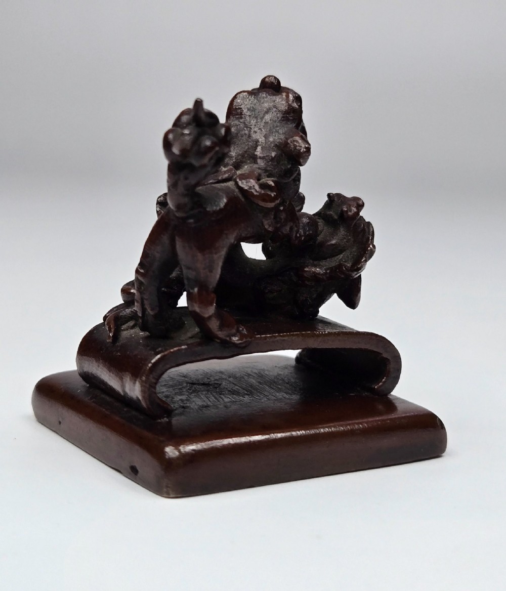 A dark bronze Chinese scholars seal topped with two sculptural wrestling shishi lions resting on an arched platform atop a square base. View IV