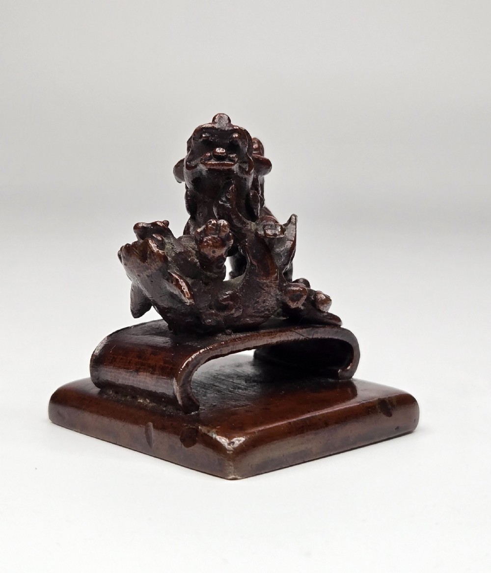 A dark bronze Chinese scholars seal topped with two sculptural wrestling shishi lions resting on an arched platform atop a square base. View IX