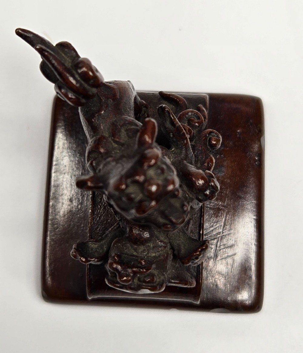 A dark bronze Chinese scholars seal topped with two sculptural wrestling shishi lions resting on an arched platform atop a square base. View XI