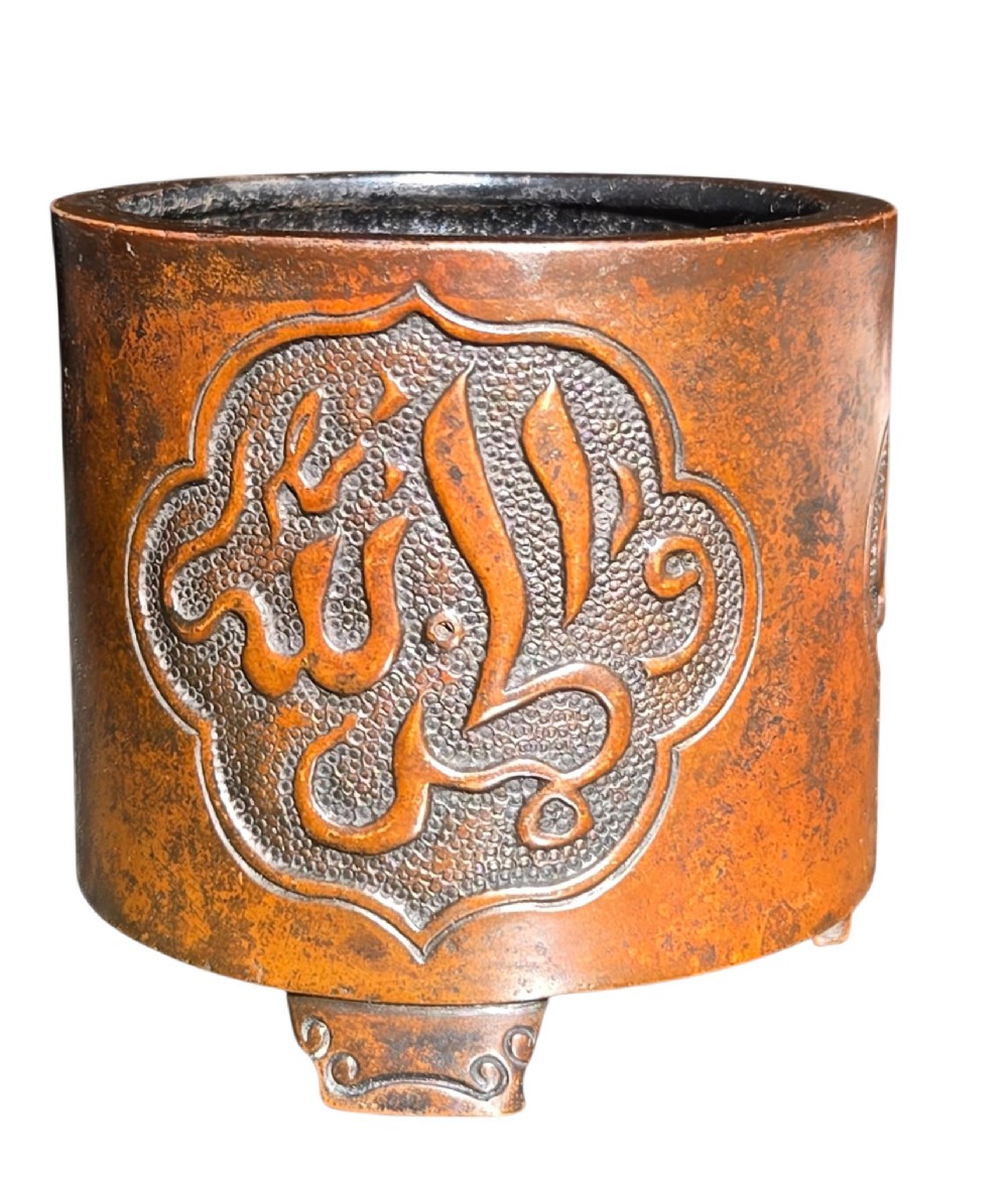 A cylindrical warm brown bronze tripod censer featuring a raised lobed cartouche with Arabic calligraphy set against a textured ground. View II