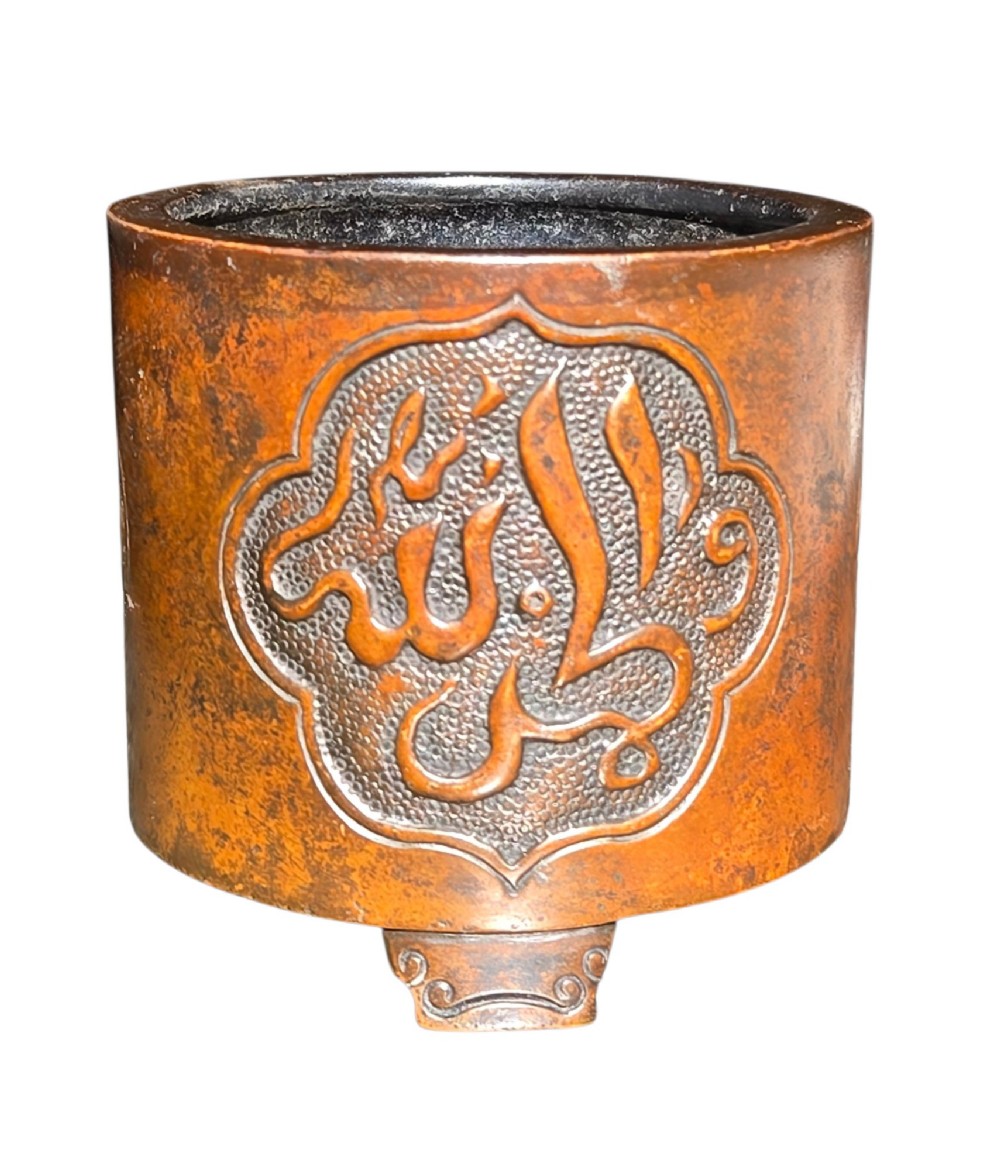 A cylindrical warm brown bronze tripod censer featuring a raised lobed cartouche with Arabic calligraphy set against a textured ground. View VIII