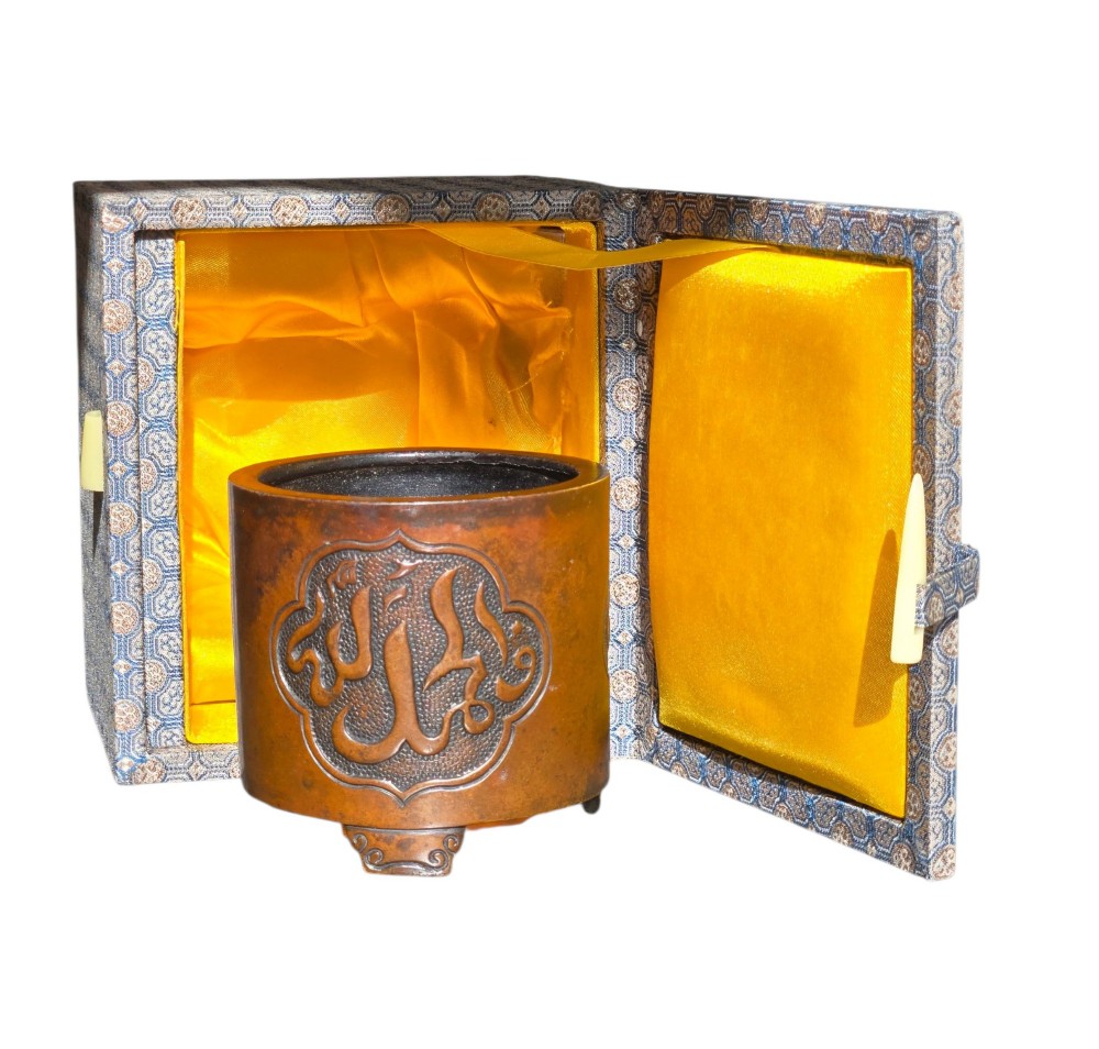A cylindrical warm brown bronze tripod censer featuring a raised lobed cartouche with Arabic calligraphy set against a textured ground. View XIV