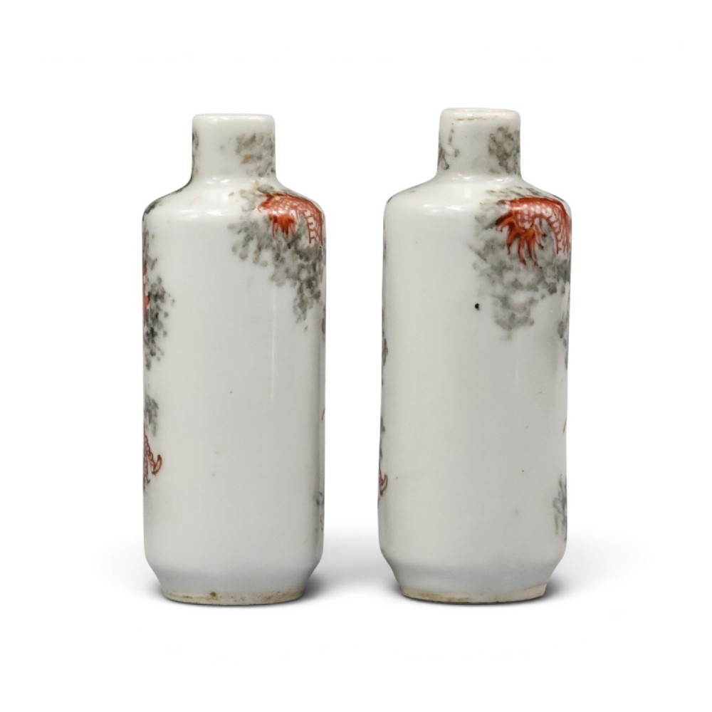 A matched pair of cylindrical off-white Chinese porcelain snuff bottles decorated with detailed iron-red dragons amongst grey clouds. View II