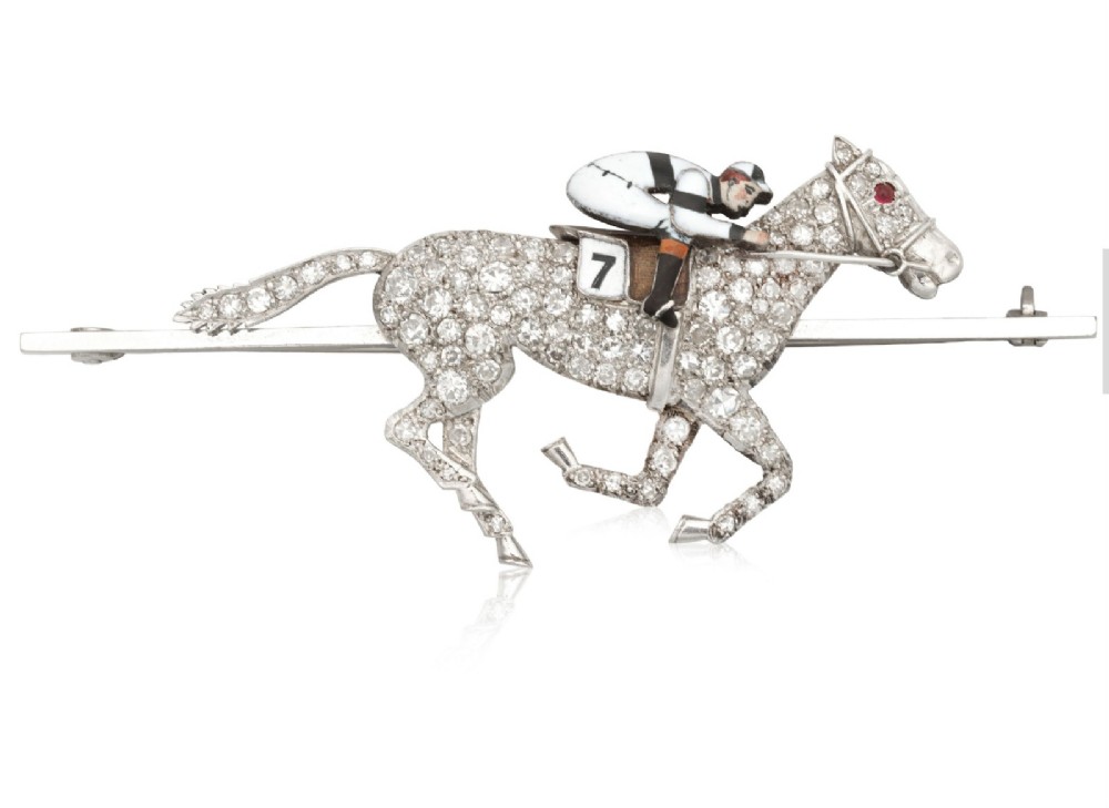 A platinum-topped 18ct gold brooch shaped as a galloping racehorse set with diamonds, ridden by a jockey in black and white enamel silks with number seven.