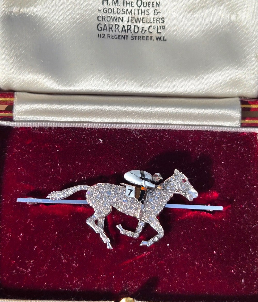 A platinum-topped 18ct gold brooch shaped as a galloping racehorse set with diamonds, ridden by a jockey in black and white enamel silks with number seven. View II