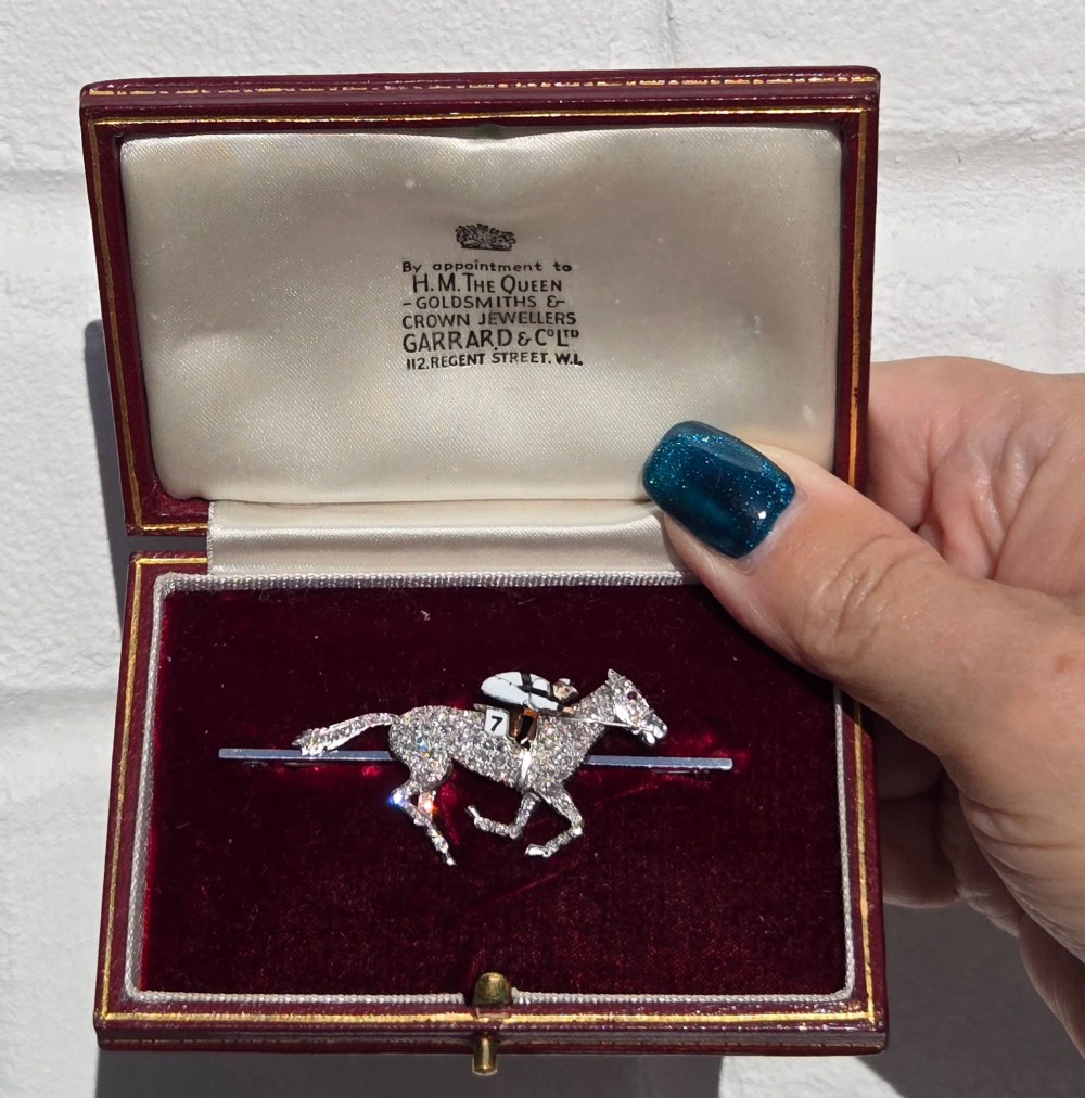 A platinum-topped 18ct gold brooch shaped as a galloping racehorse set with diamonds, ridden by a jockey in black and white enamel silks with number seven. View V