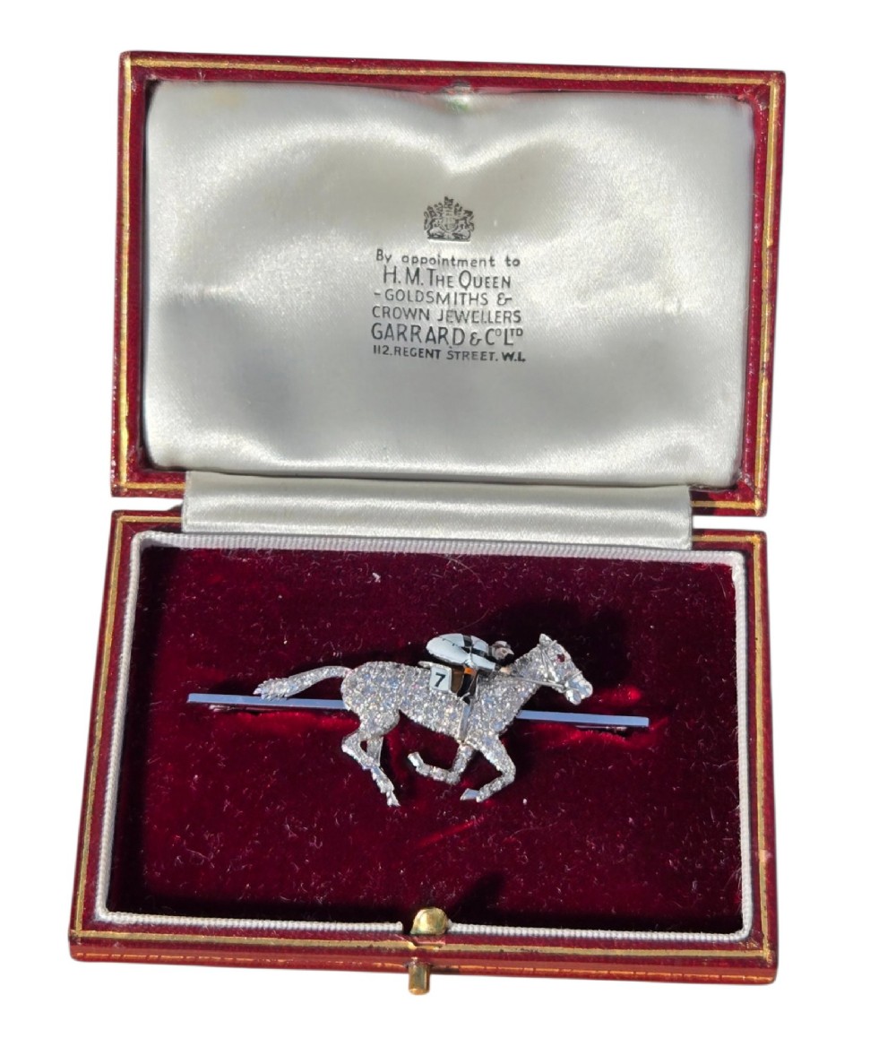 A platinum-topped 18ct gold brooch shaped as a galloping racehorse set with diamonds, ridden by a jockey in black and white enamel silks with number seven. View VI