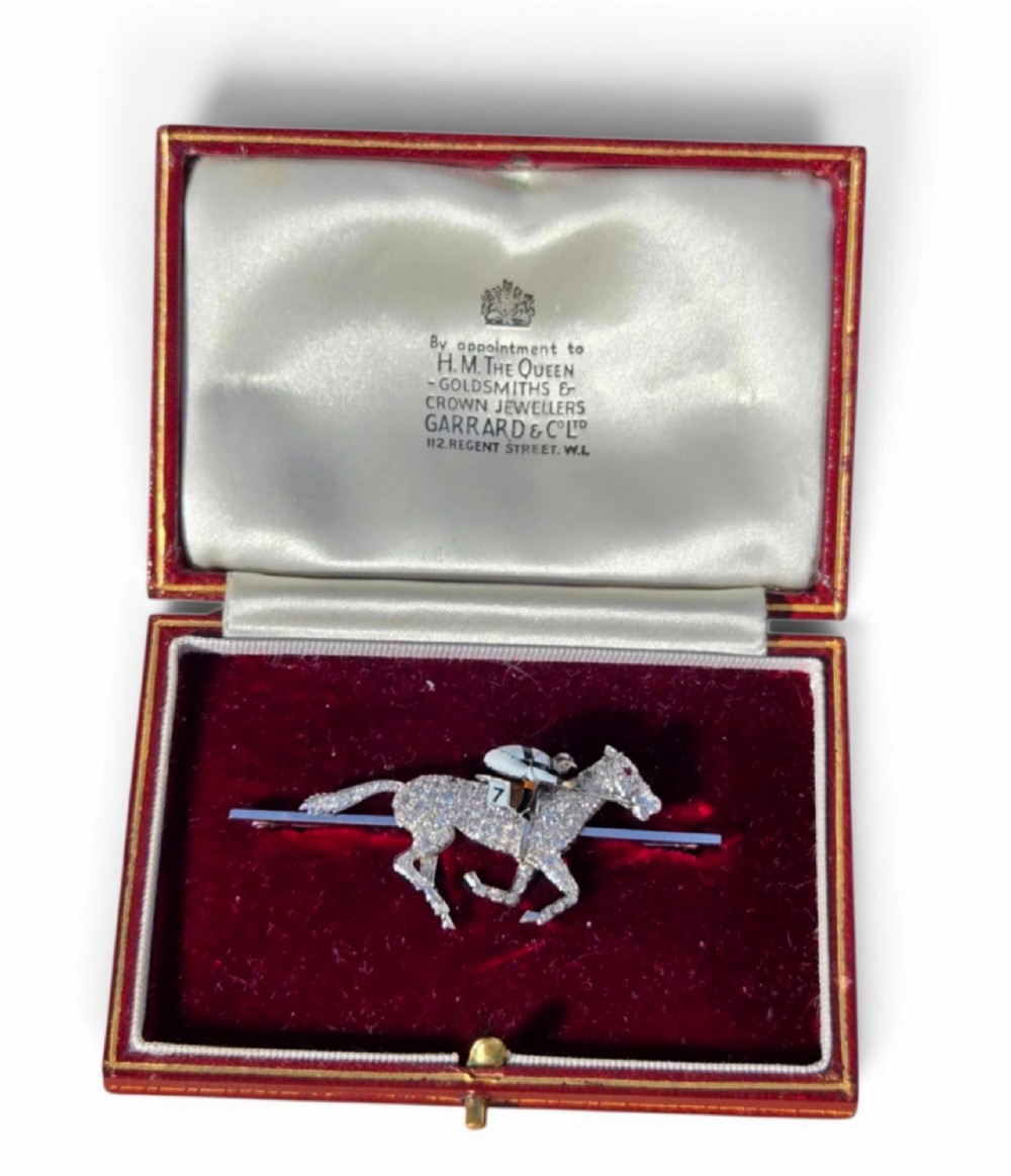 A platinum-topped 18ct gold brooch shaped as a galloping racehorse set with diamonds, ridden by a jockey in black and white enamel silks with number seven. View IX