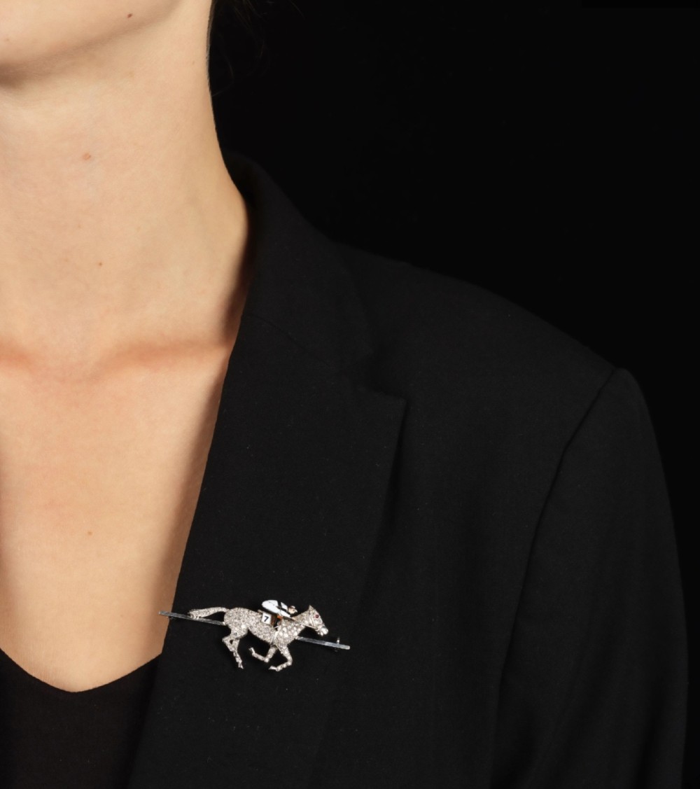 A platinum-topped 18ct gold brooch shaped as a galloping racehorse set with diamonds, ridden by a jockey in black and white enamel silks with number seven. View X