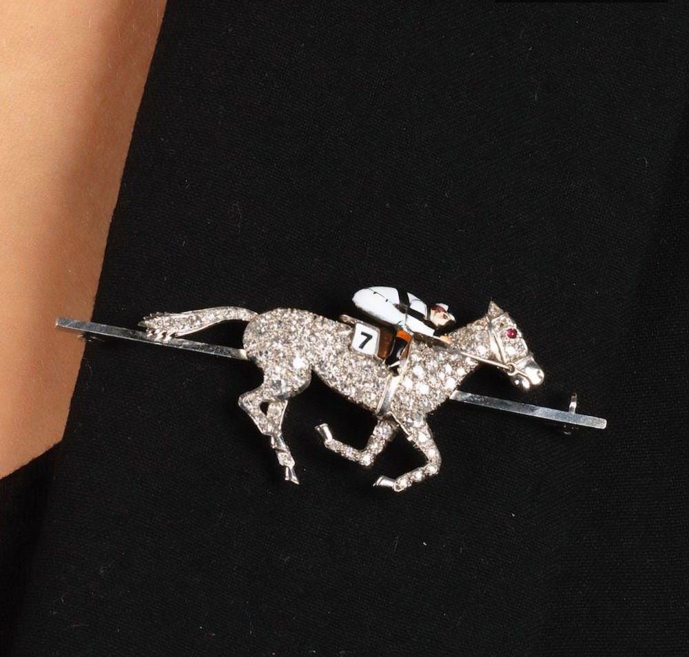 A platinum-topped 18ct gold brooch shaped as a galloping racehorse set with diamonds, ridden by a jockey in black and white enamel silks with number seven. View XI