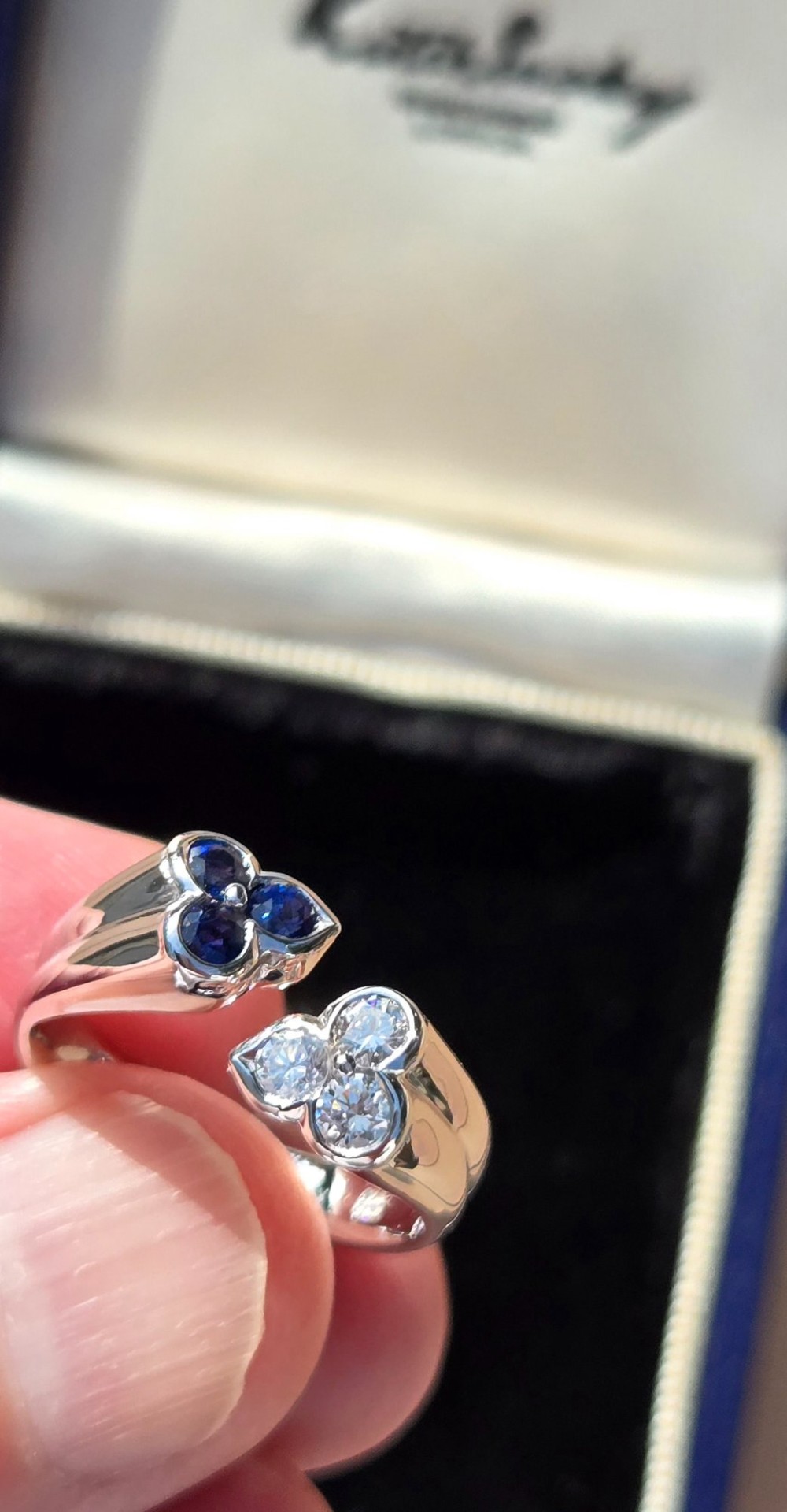 A mid-century 18ct white gold crossover ring features opposing trefoil terminals set with blue sapphires and brilliant-cut diamonds. View V