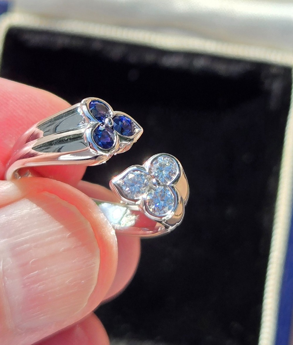 A mid-century 18ct white gold crossover ring features opposing trefoil terminals set with blue sapphires and brilliant-cut diamonds. View VI