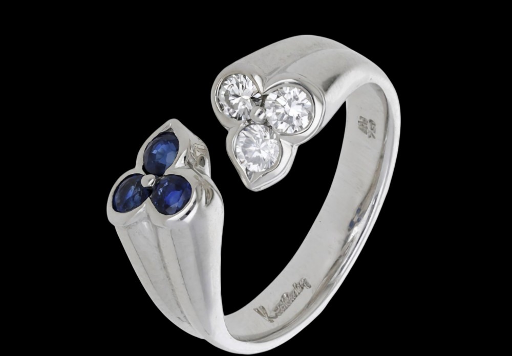 A mid-century 18ct white gold crossover ring features opposing trefoil terminals set with blue sapphires and brilliant-cut diamonds. View VII