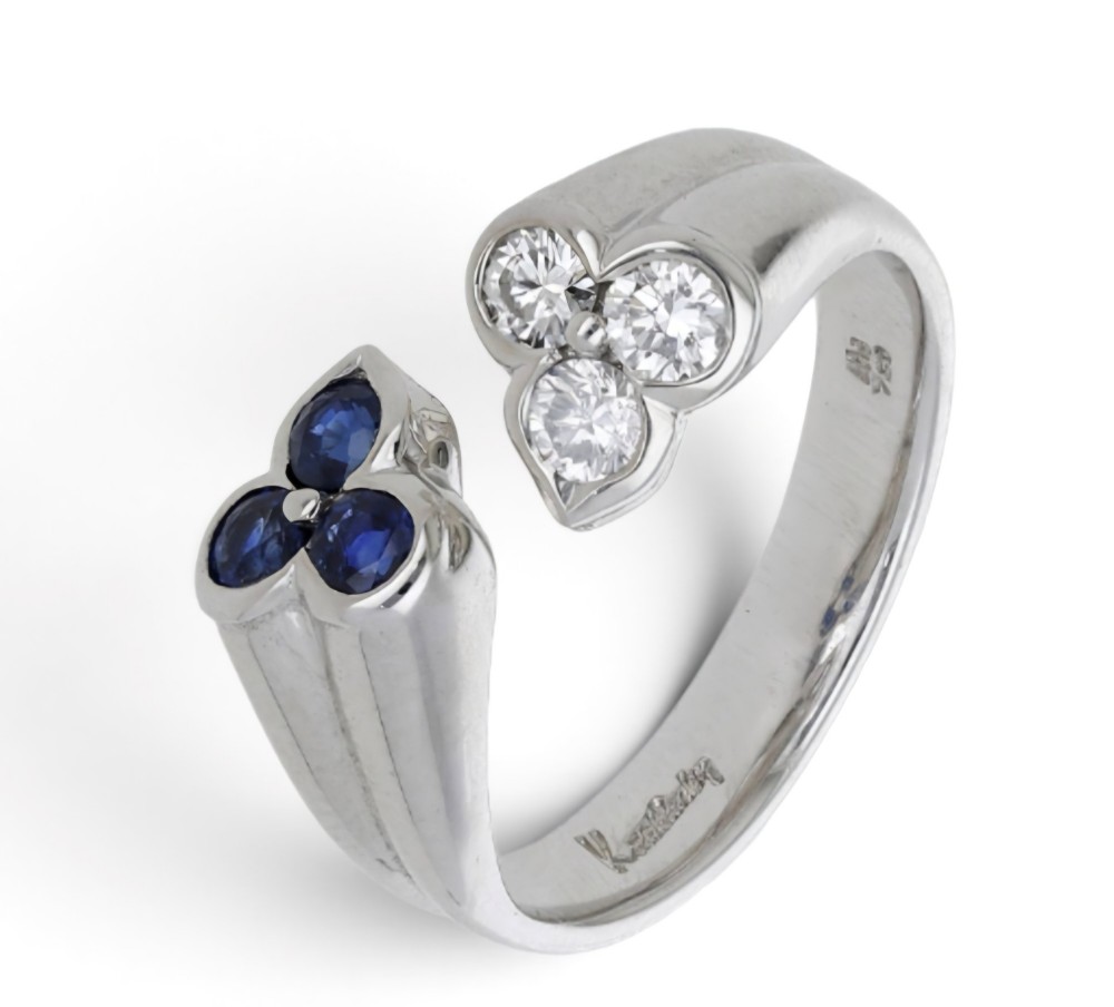 A mid-century 18ct white gold crossover ring features opposing trefoil terminals set with blue sapphires and brilliant-cut diamonds.
