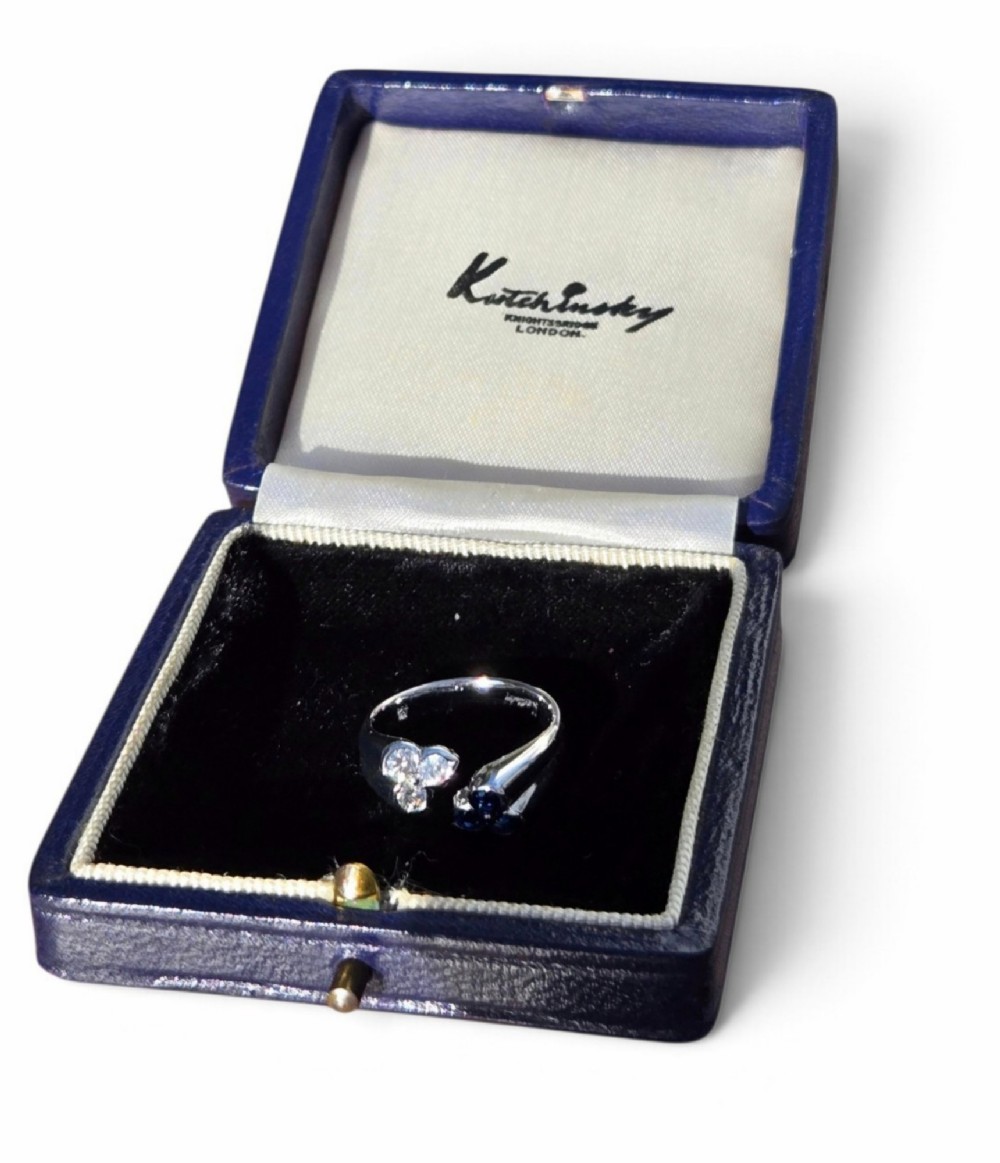 A mid-century 18ct white gold crossover ring features opposing trefoil terminals set with blue sapphires and brilliant-cut diamonds. View IX