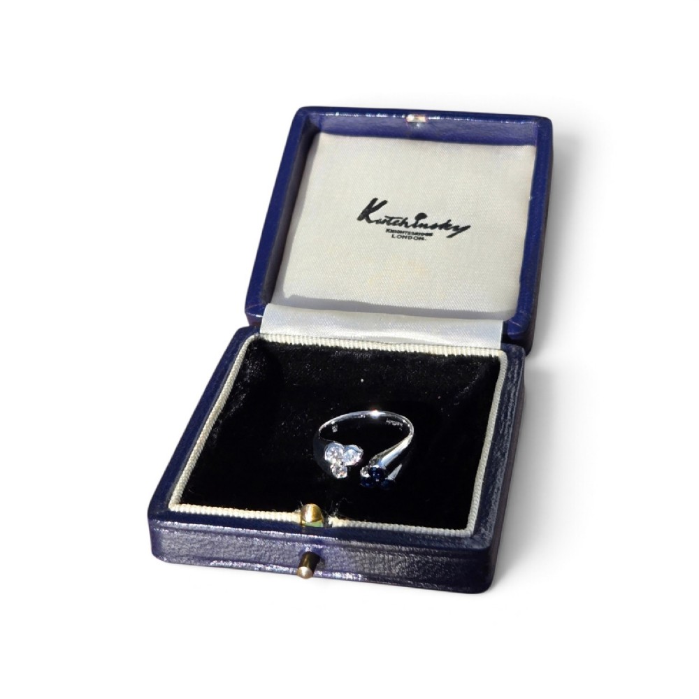 A mid-century 18ct white gold crossover ring features opposing trefoil terminals set with blue sapphires and brilliant-cut diamonds. View X