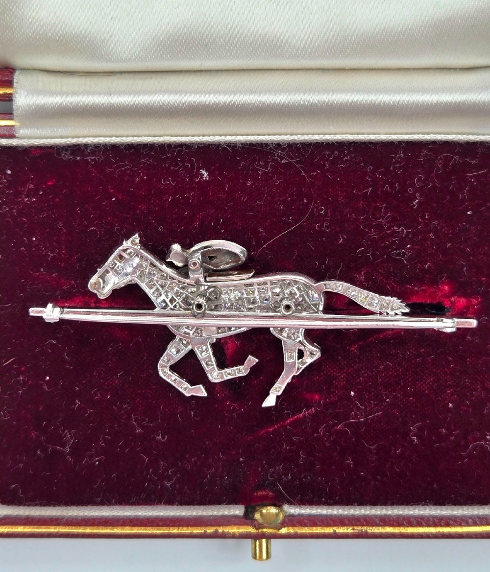A platinum-topped 18ct gold brooch shaped as a galloping racehorse set with diamonds, ridden by a jockey in black and white enamel silks with number seven. View XII