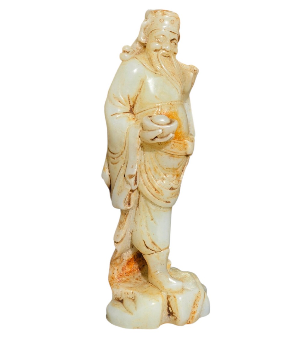 A carved pale celadon and russet nephrite jade standing figure of an immortal holding a vessel on a carved rockwork base. View III