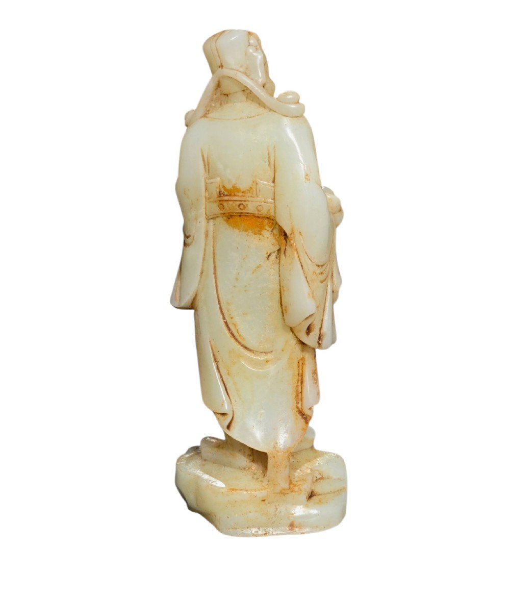 A carved pale celadon and russet nephrite jade standing figure of an immortal holding a vessel on a carved rockwork base. View V