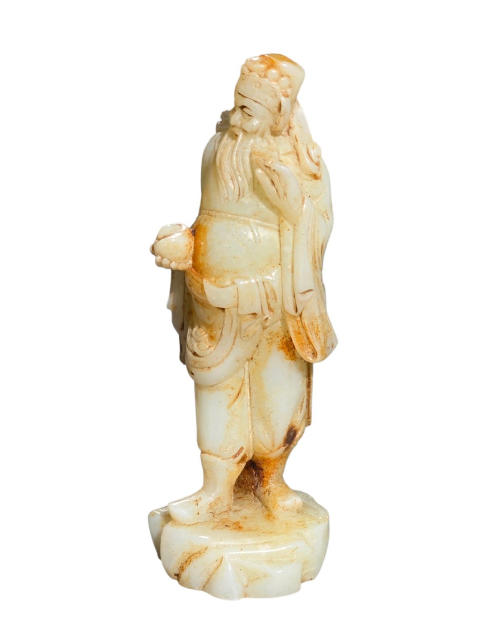 A carved pale celadon and russet nephrite jade standing figure of an immortal holding a vessel on a carved rockwork base. View VIII