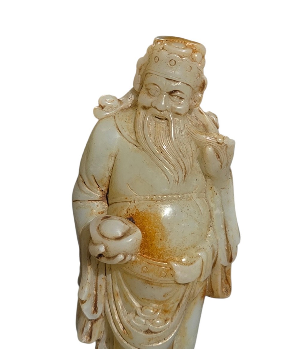 A carved pale celadon and russet nephrite jade standing figure of an immortal holding a vessel on a carved rockwork base. View XI