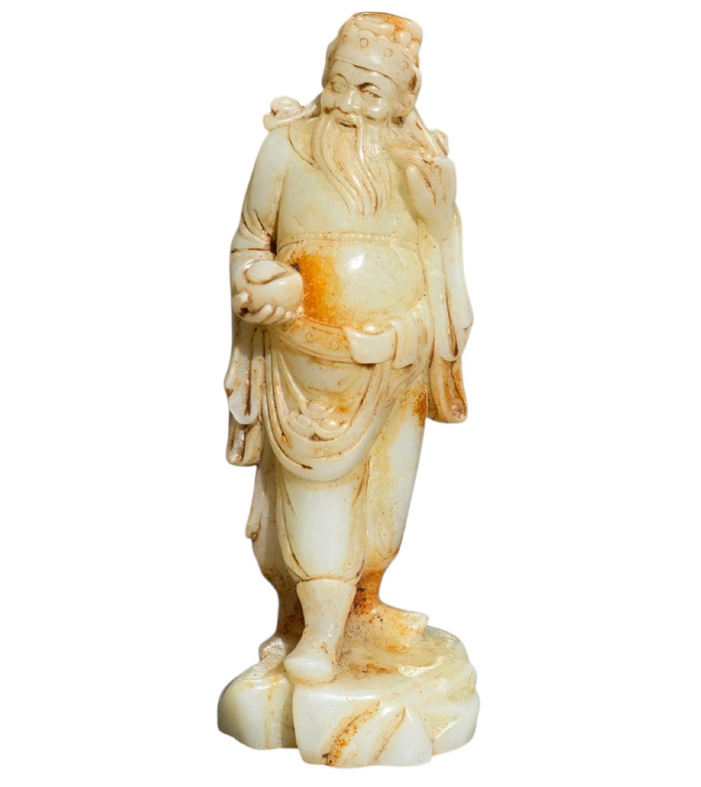 A carved pale celadon and russet nephrite jade standing figure of an immortal holding a vessel on a carved rockwork base. View XIV