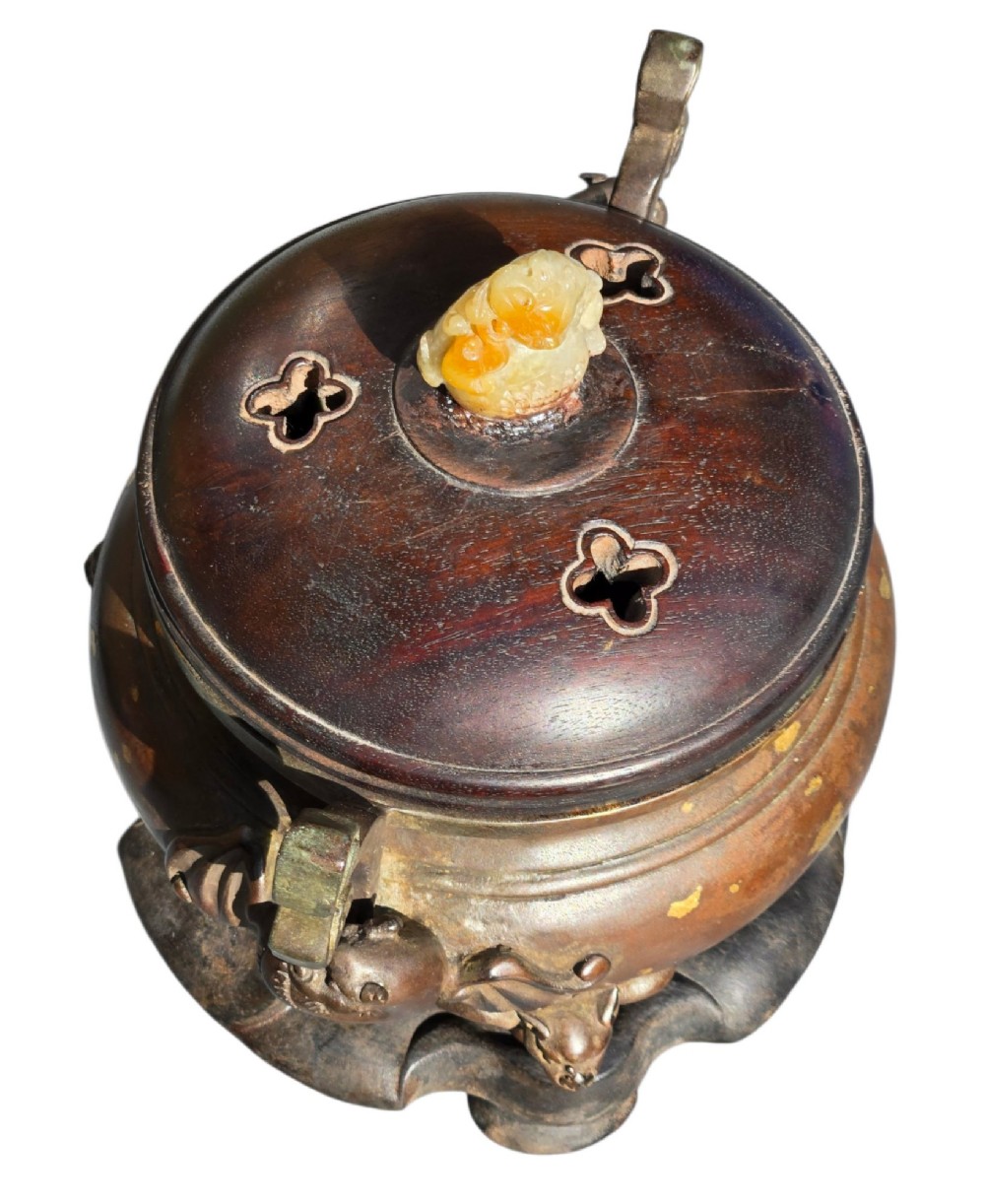 An 18th-century Chinese gilt-splashed bronze tripod censer featuring scroll handles, animal-mask legs, a dark hardwood cover topped with a carved jade finial, and a fitted bronze stand. View II