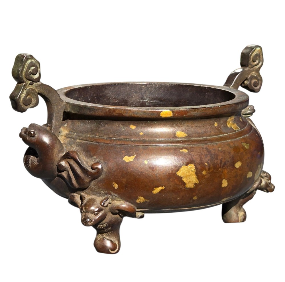 An 18th-century Chinese gilt-splashed bronze tripod censer featuring scroll handles, animal-mask legs, a dark hardwood cover topped with a carved jade finial, and a fitted bronze stand. View V