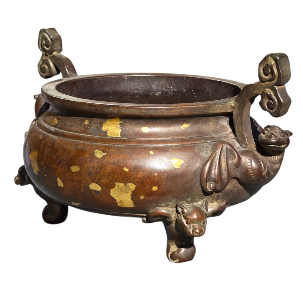 An 18th-century Chinese gilt-splashed bronze tripod censer featuring scroll handles, animal-mask legs, a dark hardwood cover topped with a carved jade finial, and a fitted bronze stand. View VI