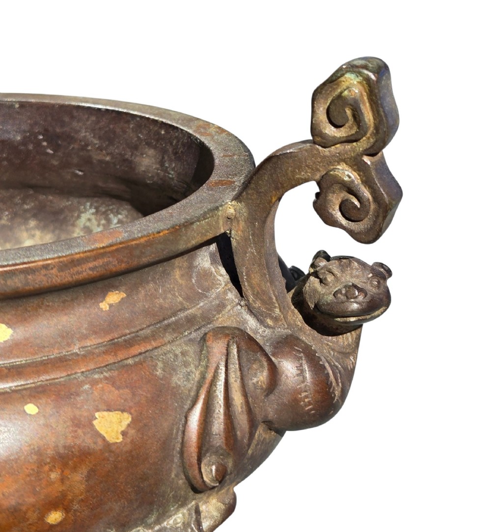 An 18th-century Chinese gilt-splashed bronze tripod censer featuring scroll handles, animal-mask legs, a dark hardwood cover topped with a carved jade finial, and a fitted bronze stand. View IX