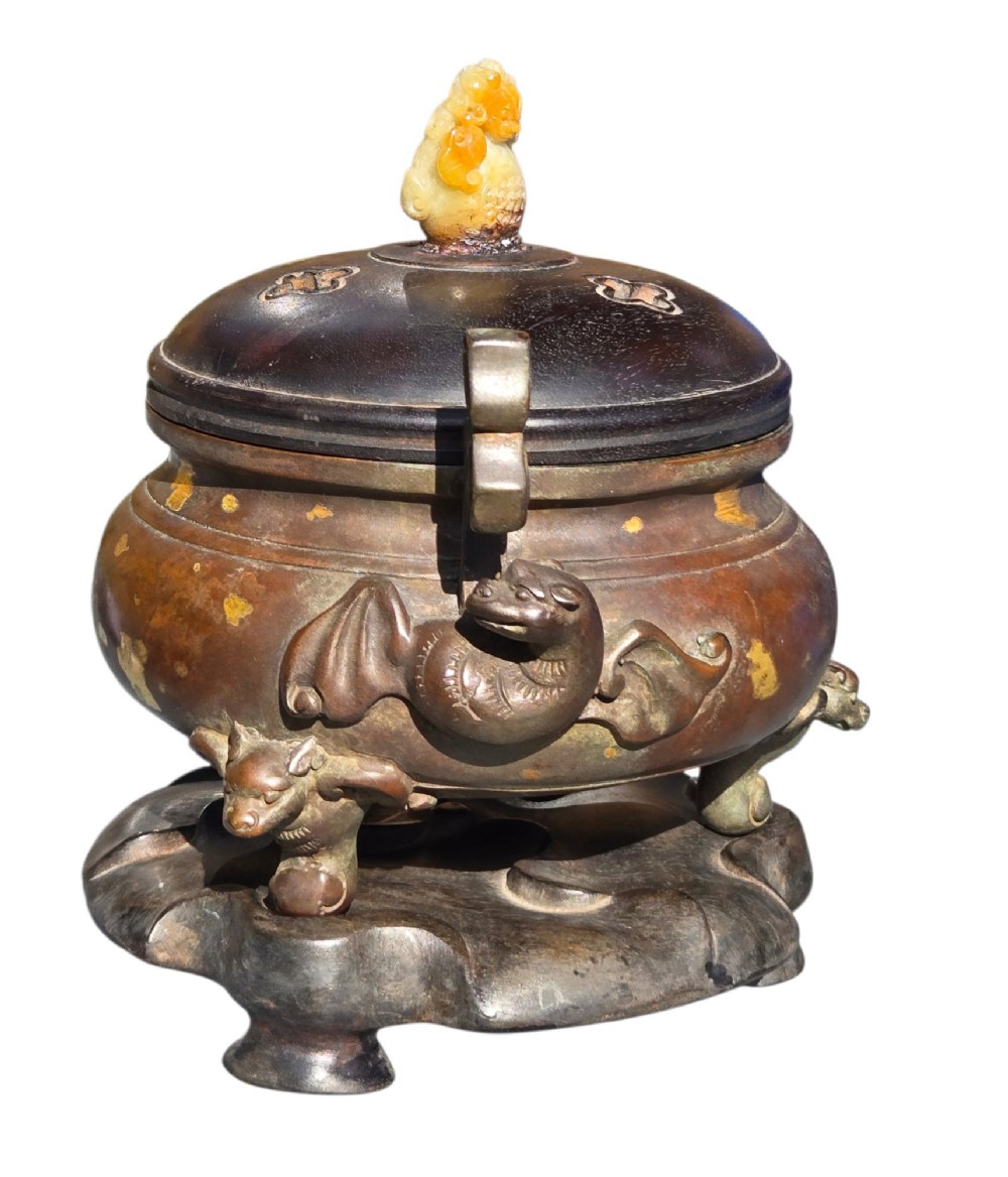 An 18th-century Chinese gilt-splashed bronze tripod censer featuring scroll handles, animal-mask legs, a dark hardwood cover topped with a carved jade finial, and a fitted bronze stand. View XI