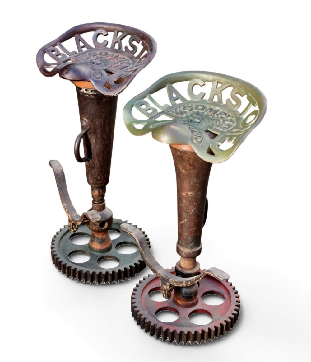 A pair of heavy industrial bar stools constructed with embossed Blackstone and Company cast-iron tractor seats, central metal columns with integrated footrests, and heavy gear cog bases. View III