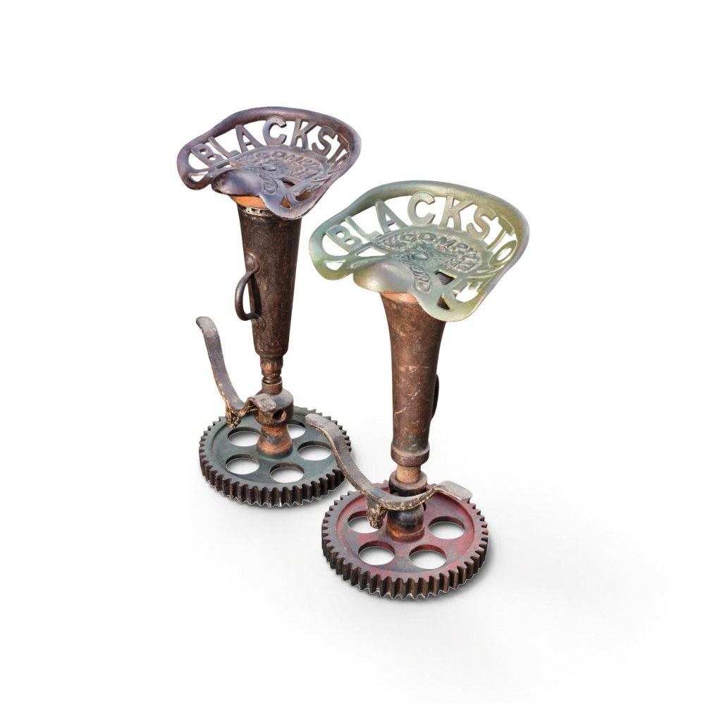 A pair of heavy industrial bar stools constructed with embossed Blackstone and Company cast-iron tractor seats, central metal columns with integrated footrests, and heavy gear cog bases. View IV
